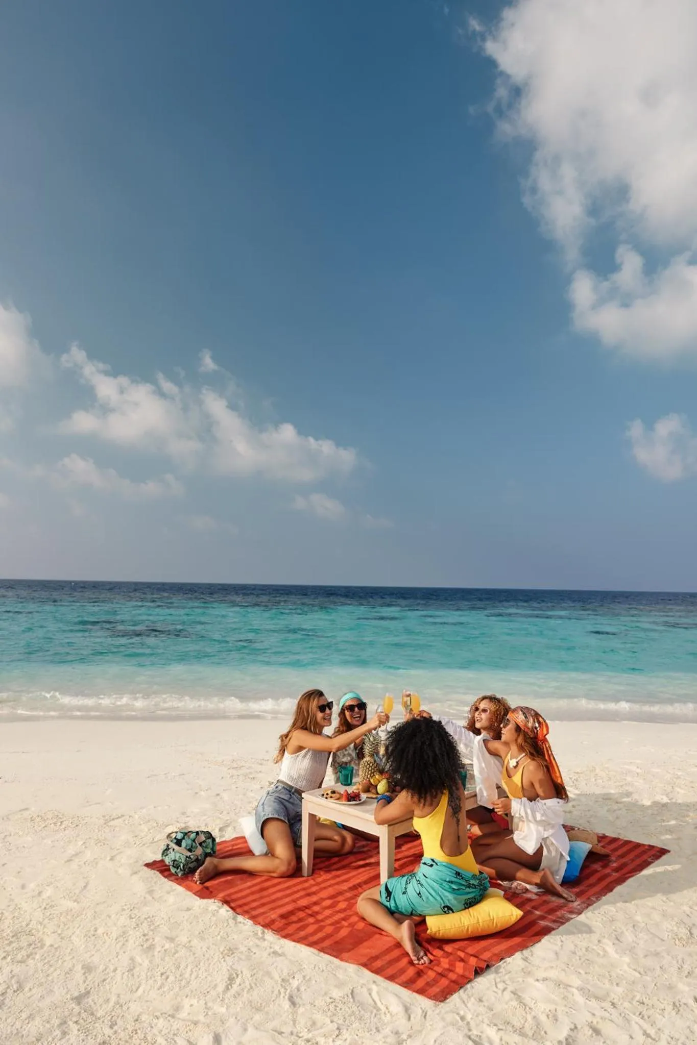 Un groupe de personnes est assis sur une plage de sable blanc, profitant de boissons et de collations.