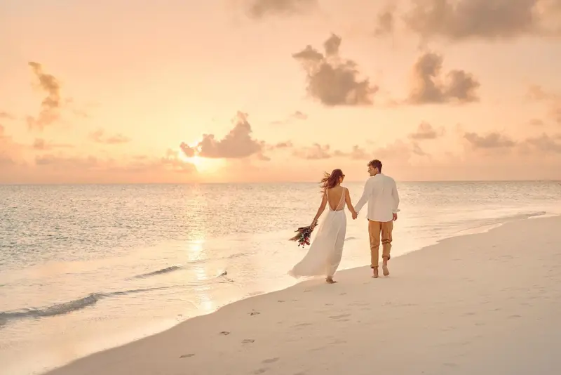 Un couple se promène sur une plage de sable blanc au coucher du soleil.