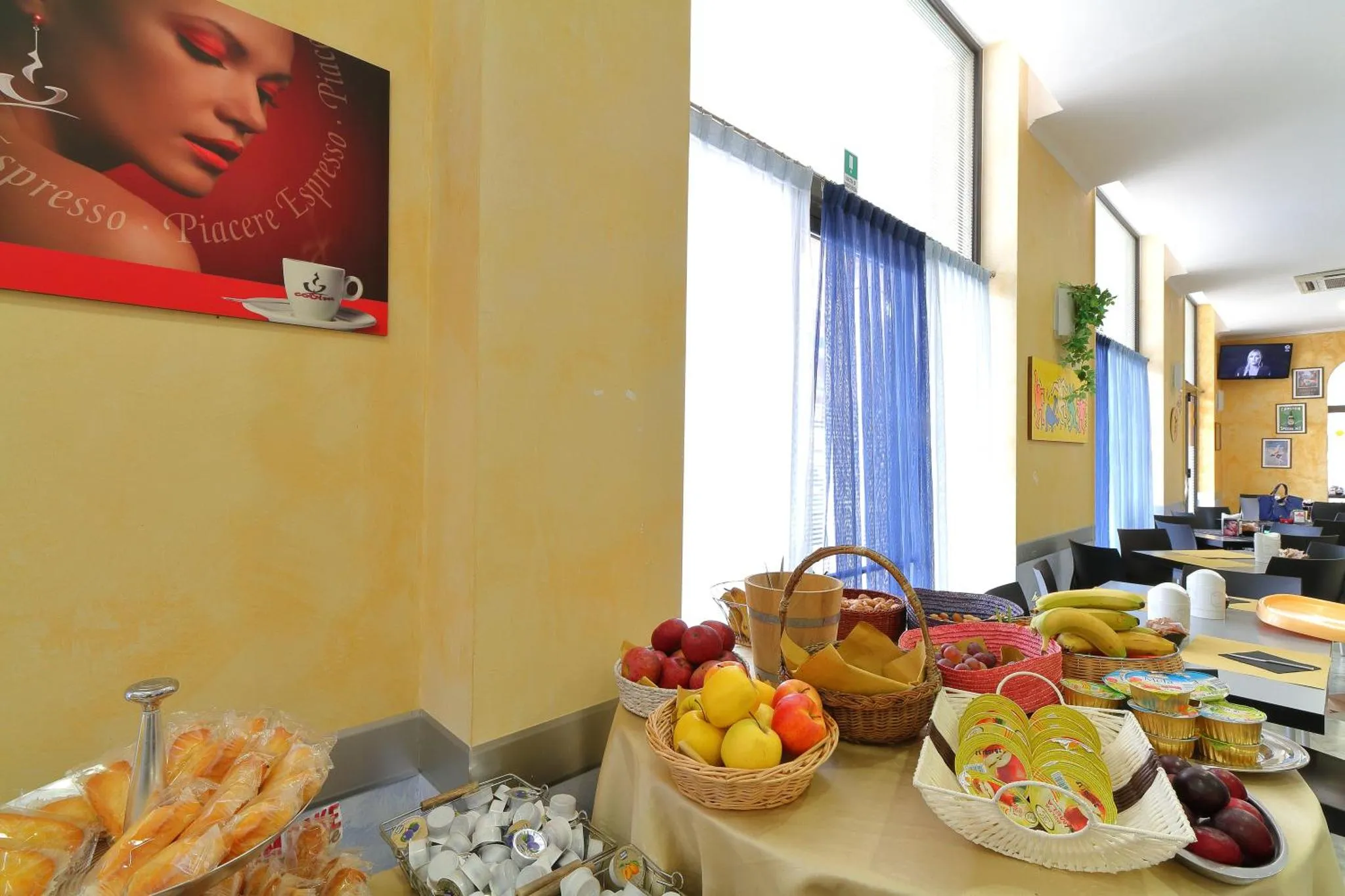 Une table garnie de fruits et de viennoiseries se trouve dans une salle lumineuse.