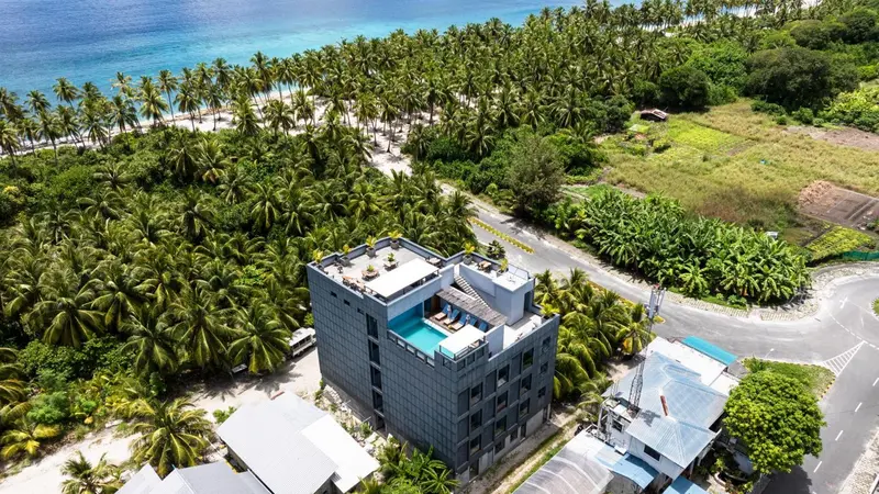Vue aérienne d'un bâtiment moderne avec une piscine sur le toit, entouré de végétation tropicale et d'une plage.
