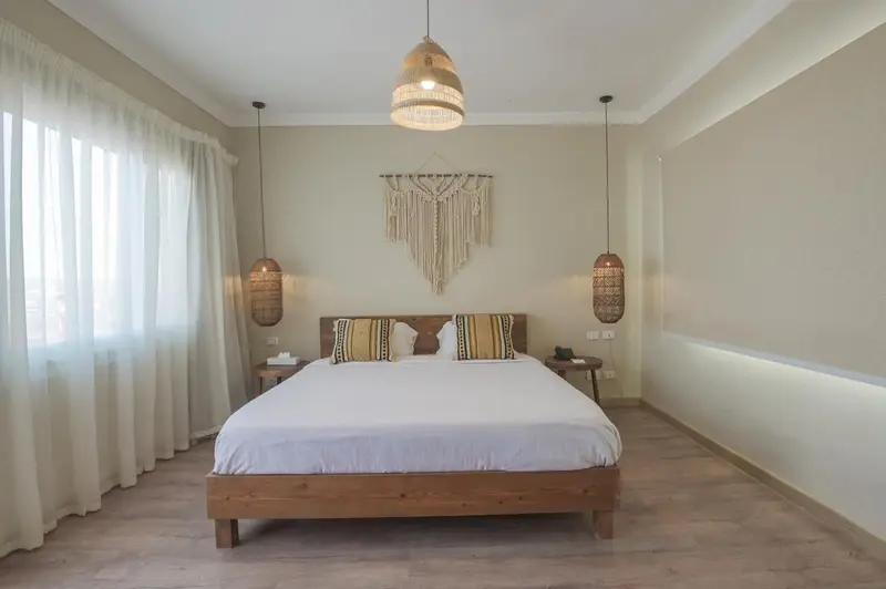 Une chambre lumineuse avec un grand lit et une décoration murale en macramé.