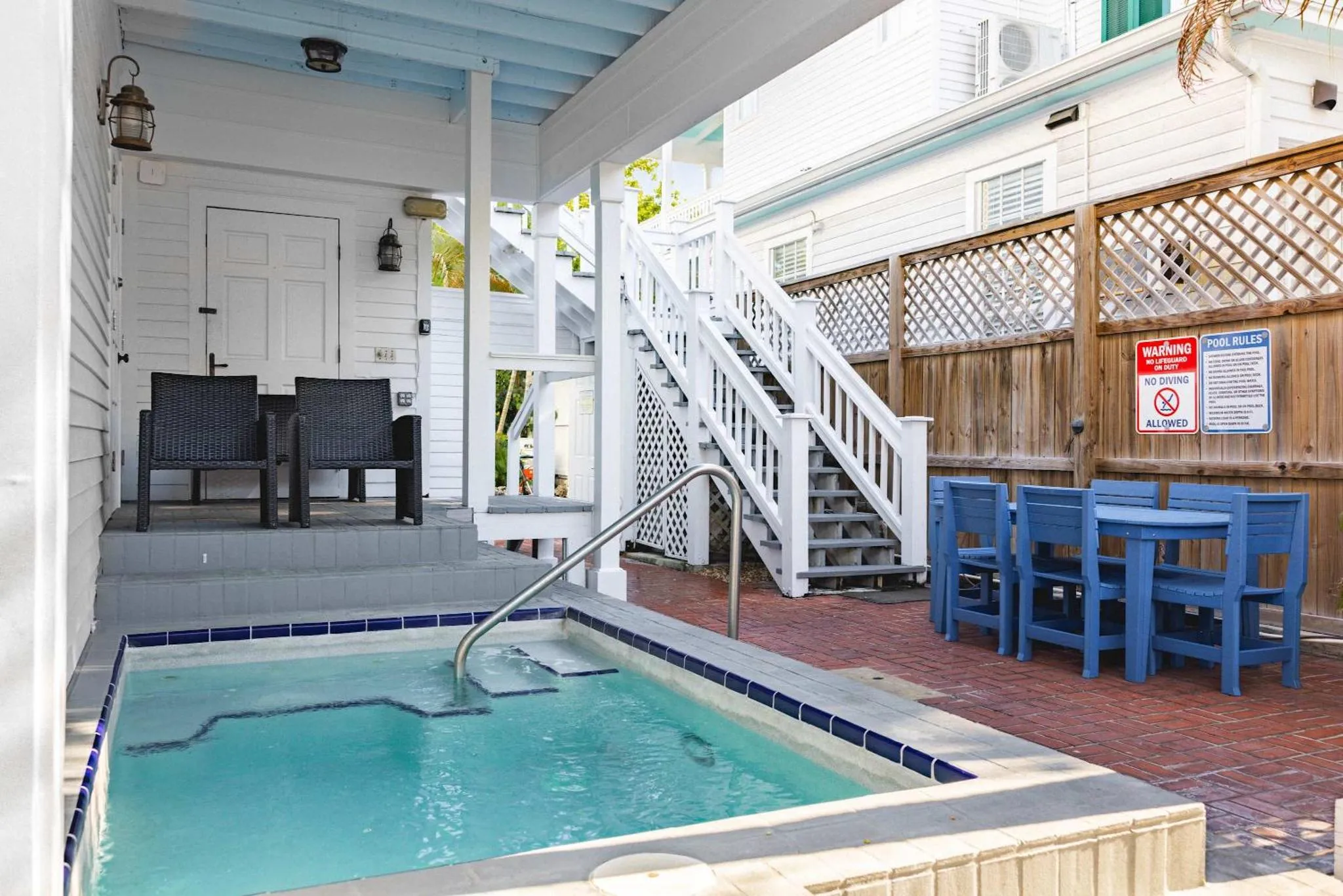 Petite piscine rectangulaire entourée d'une terrasse pavée et de mobilier de jardin bleu.
