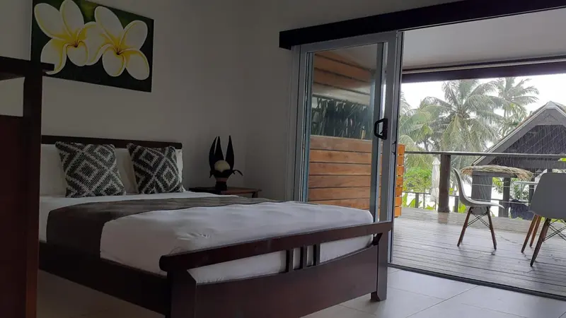 Une chambre avec un lit fait et un accès à une terrasse en bois.