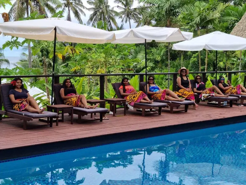Des femmes se relaxent sur des chaises longues au bord d'une piscine turquoise.