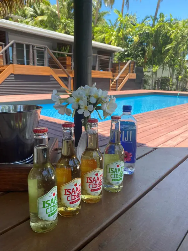 Une table en bois avec des bouteilles et des boissons près d'une piscine ensoleillée.
