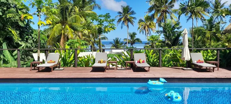 Transats alignés au bord d'une piscine turquoise, végétation luxuriante en arrière-plan.