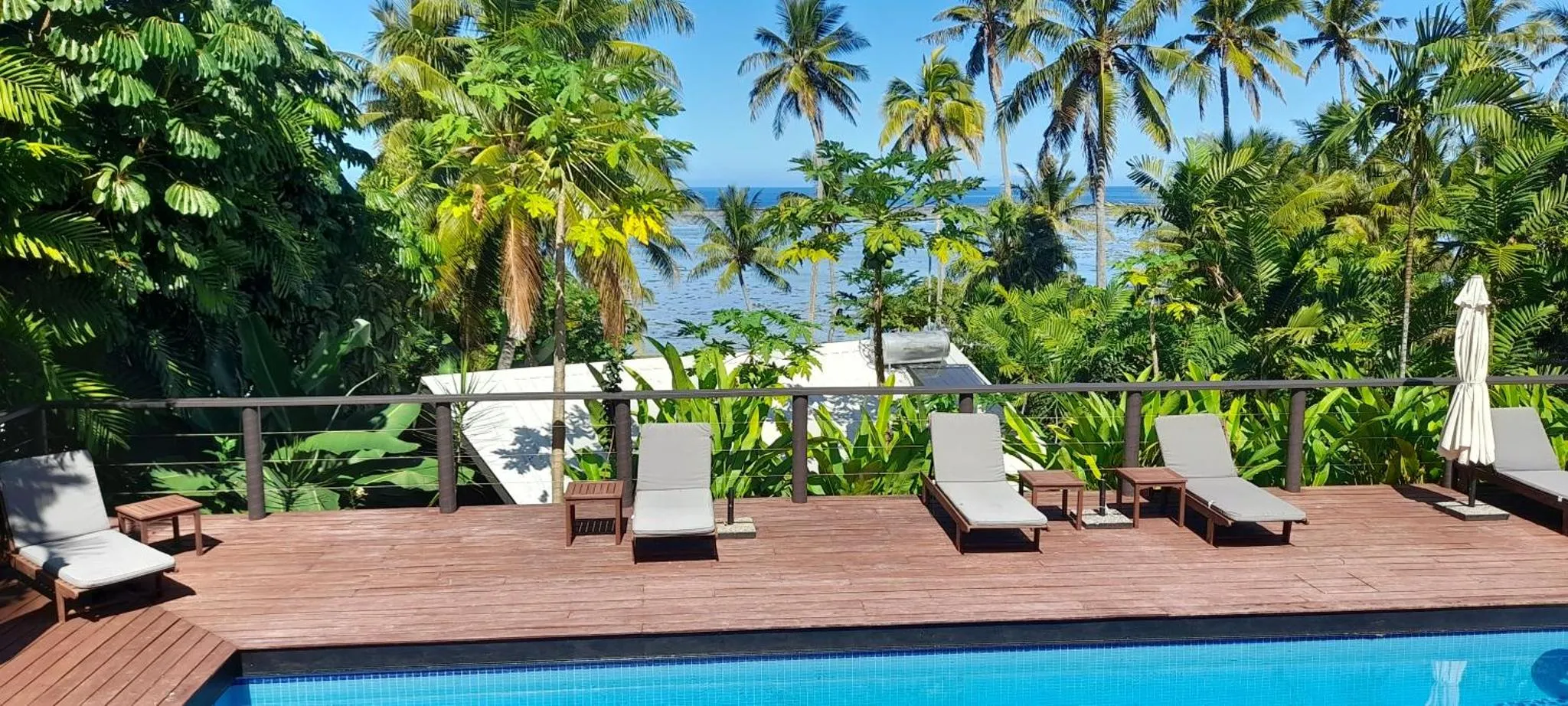 Terrasse en bois avec transats et piscine donnant sur la mer et la végétation tropicale.