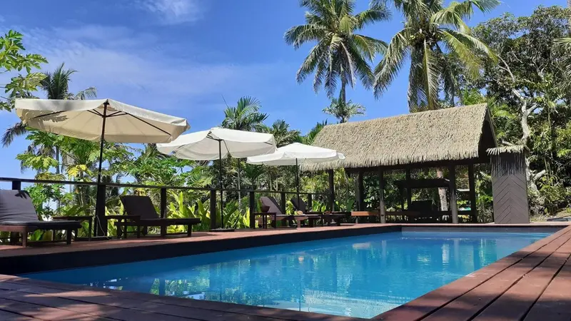 Une piscine turquoise bordée d'une terrasse en bois avec des transats et des parasols.