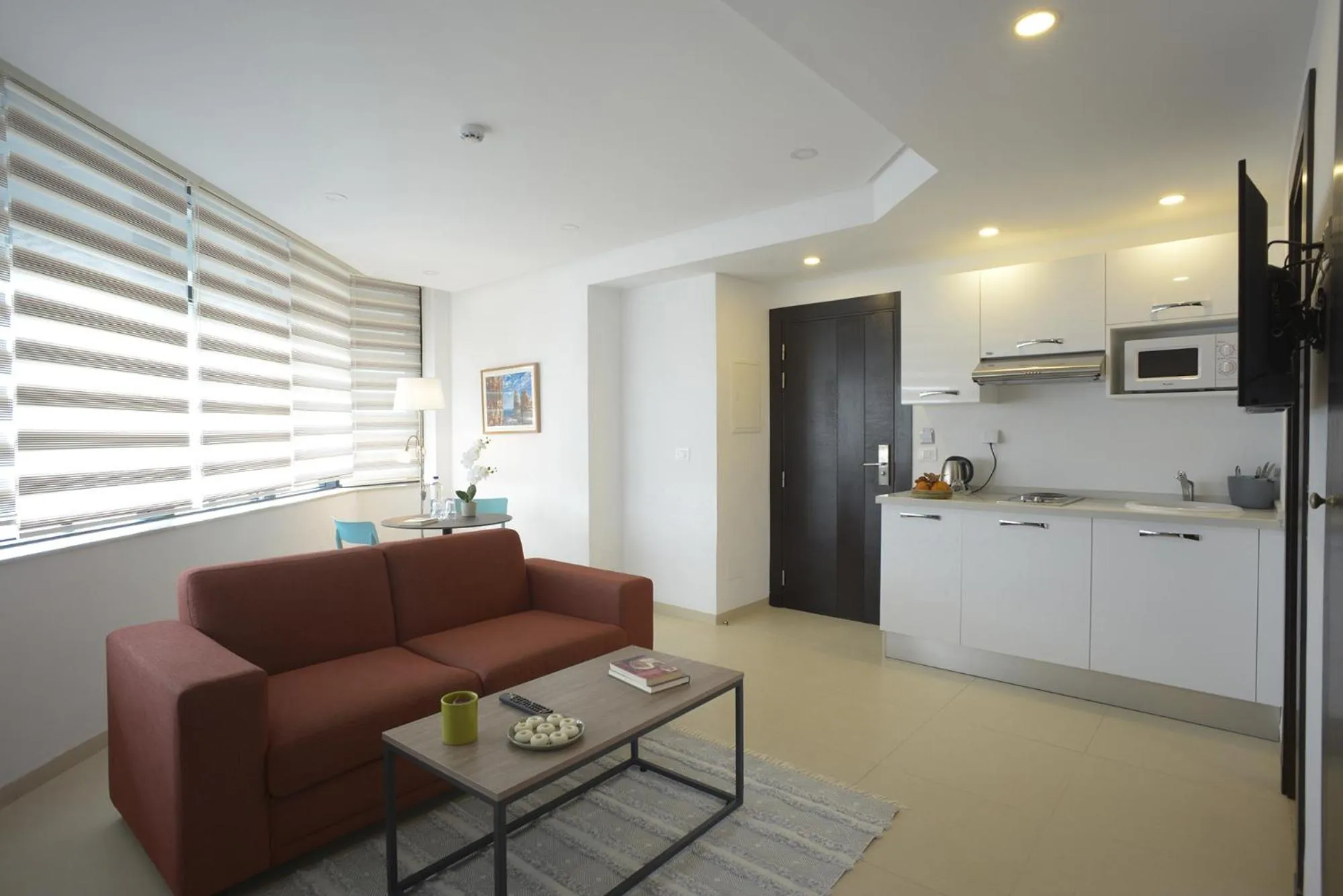 Espace de vie lumineux avec canapé rouge et cuisine équipée.