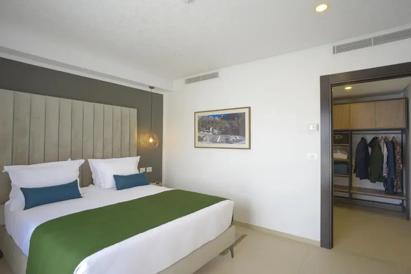 Une chambre lumineuse avec un grand lit et un dressing ouvert.