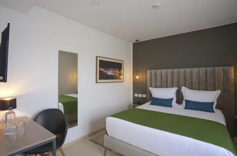 Une chambre lumineuse avec un grand lit recouvert d'une couette verte et de coussins bleus.