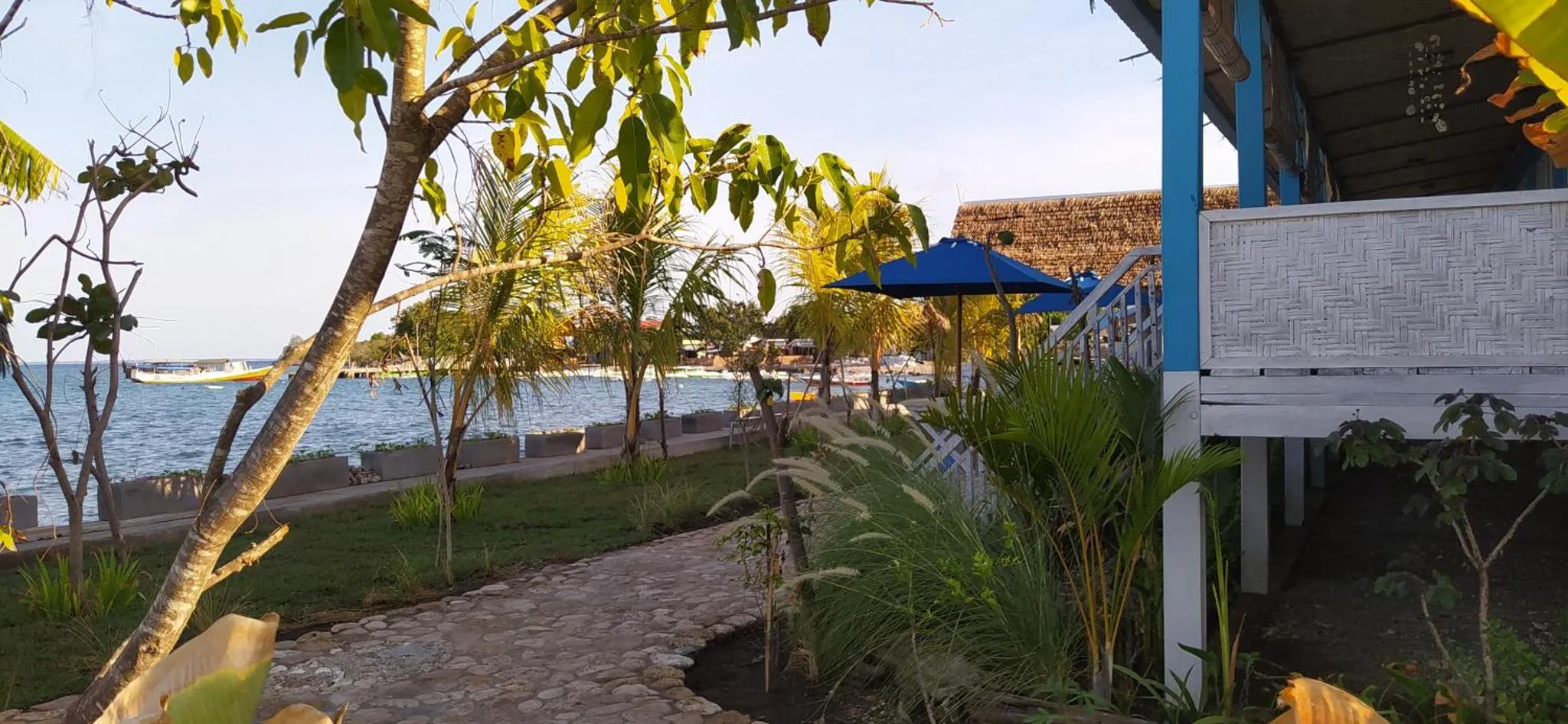 Terrasse en bois avec mobilier de jardin donnant sur la mer et la végétation tropicale.