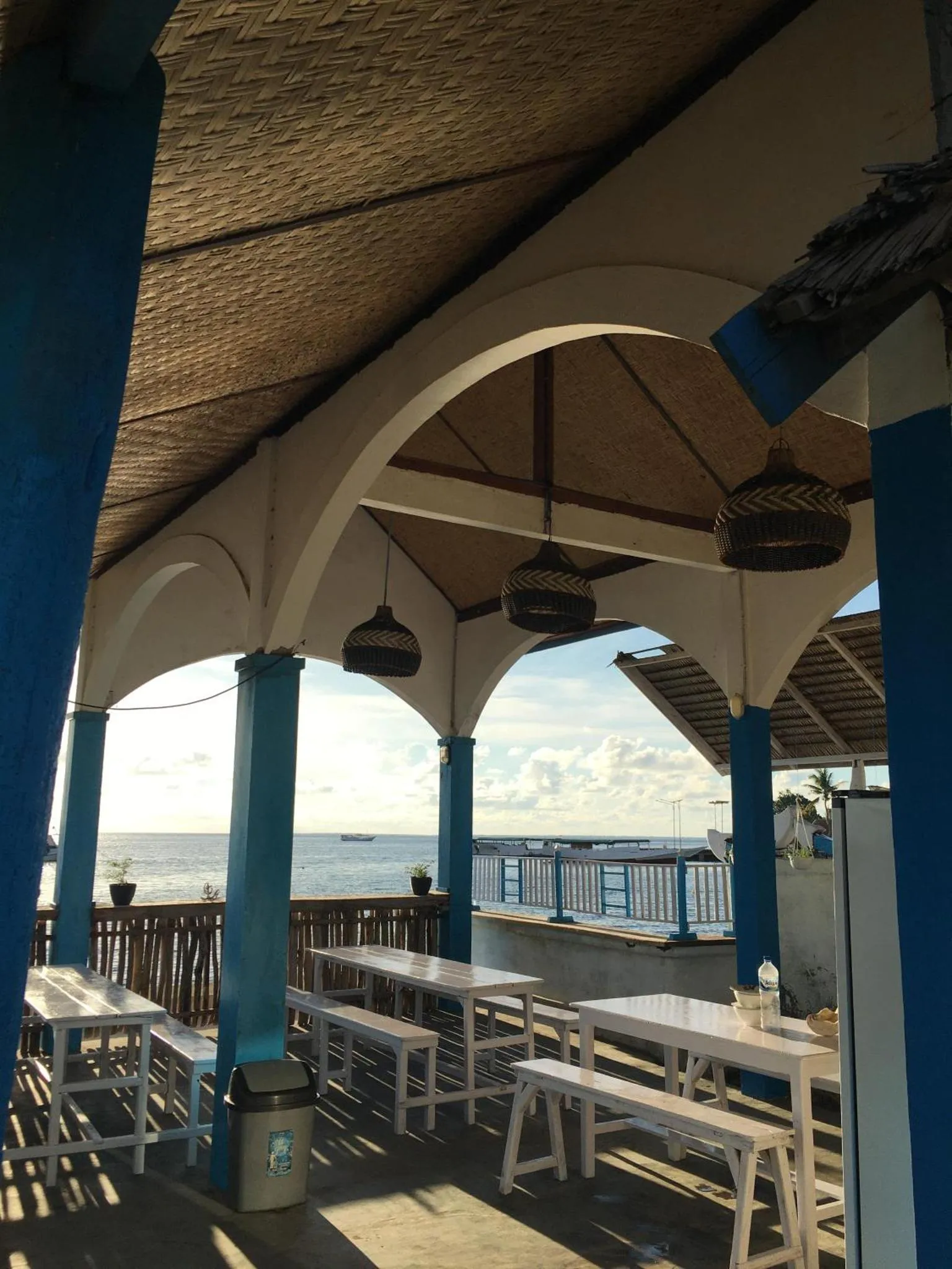 Terrasse ombragée avec tables et chaises donnant sur la mer.