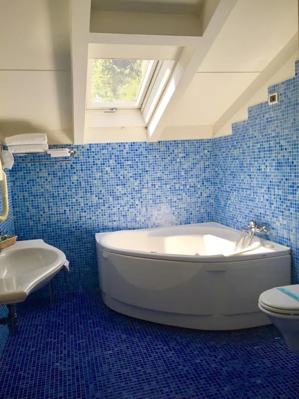Une salle de bain lumineuse avec une baignoire d'angle et des murs recouverts de mosaïque bleue.