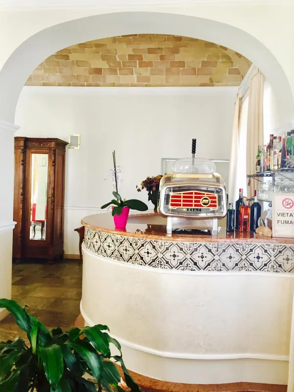 Un comptoir de bar décoré de motifs géométriques accueille une machine à expresso et des bouteilles.