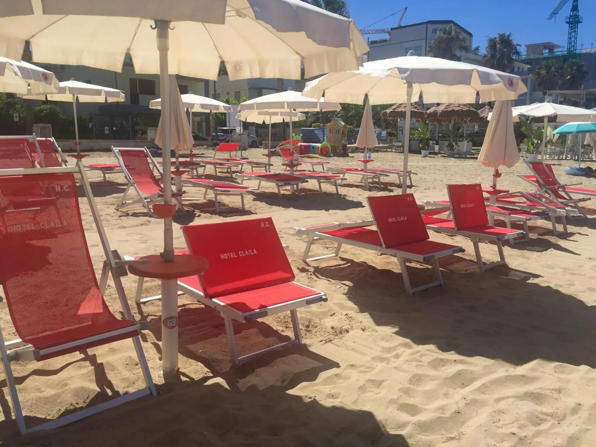 Transats rouges alignés sur une plage de sable fin sous des parasols blancs.