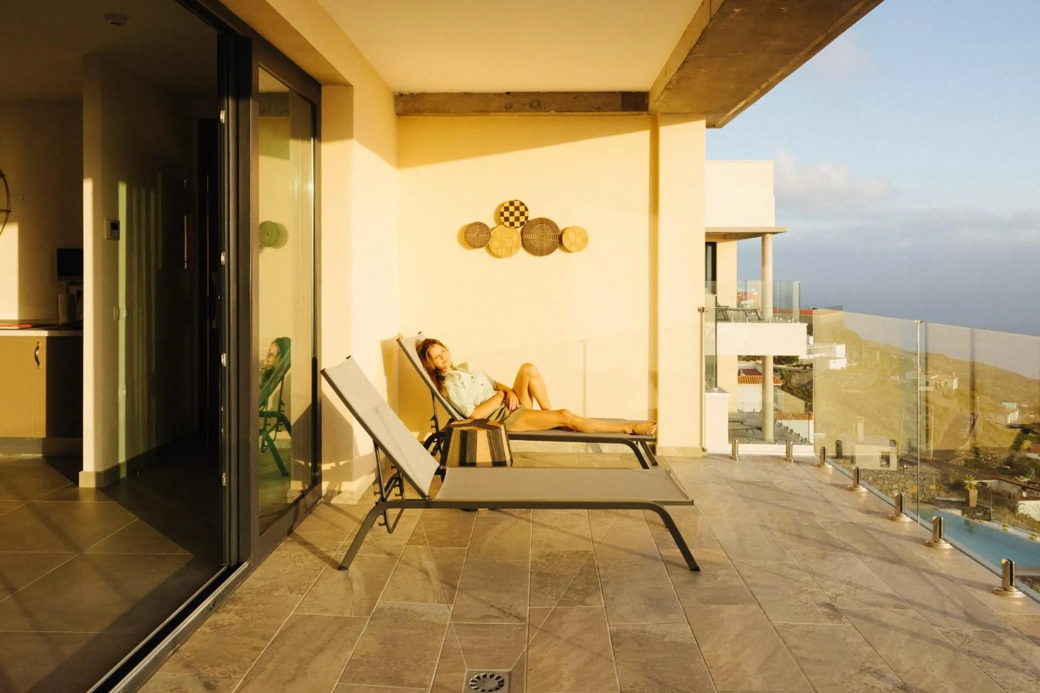 Une personne se relaxe sur une chaise longue sur une terrasse ensoleillée avec vue sur la mer.