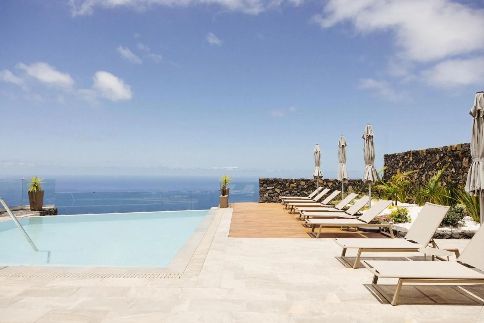 Transats blancs alignés au bord d'une piscine à débordement avec vue sur la mer.