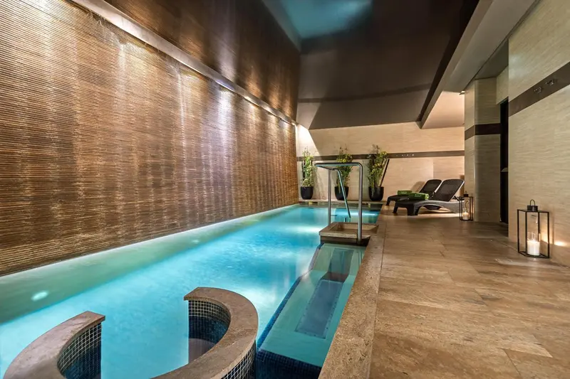 Une piscine intérieure illuminée avec un mur texturé et des chaises longues.