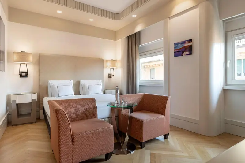 Chambre lumineuse avec un lit double et deux fauteuils.