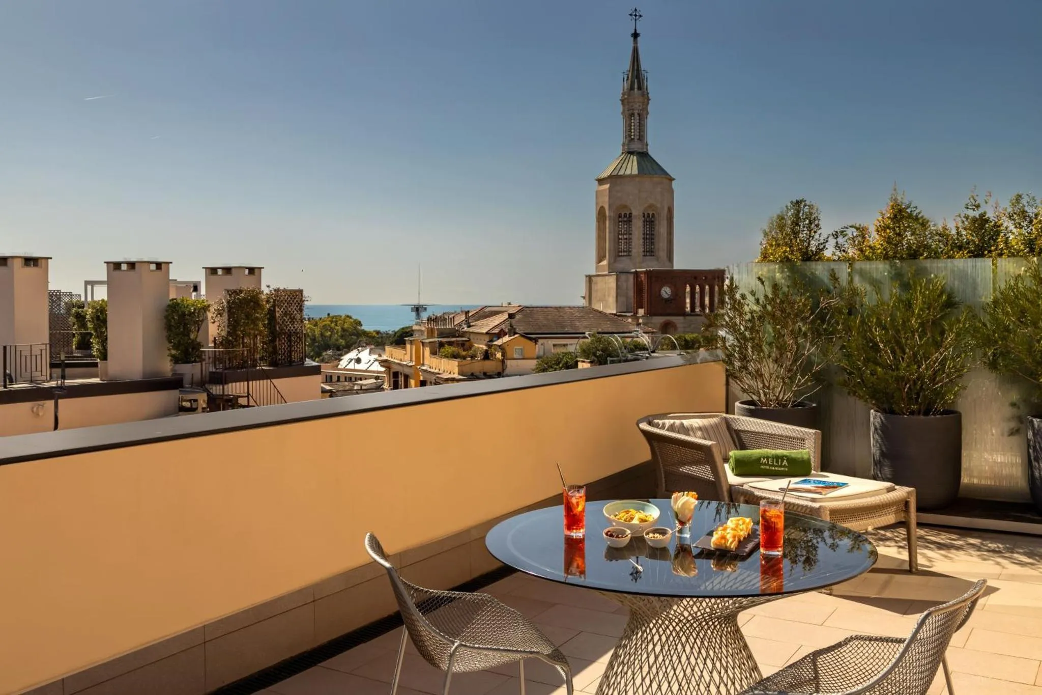 Une table ronde avec des boissons et des en-cas sur une terrasse ensoleillée avec vue sur la ville.