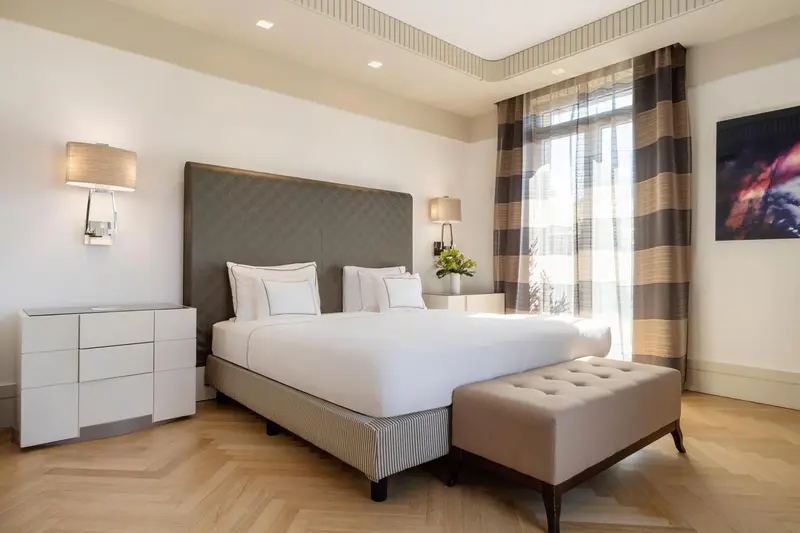 Une chambre lumineuse avec un grand lit et un banc au pied du lit.