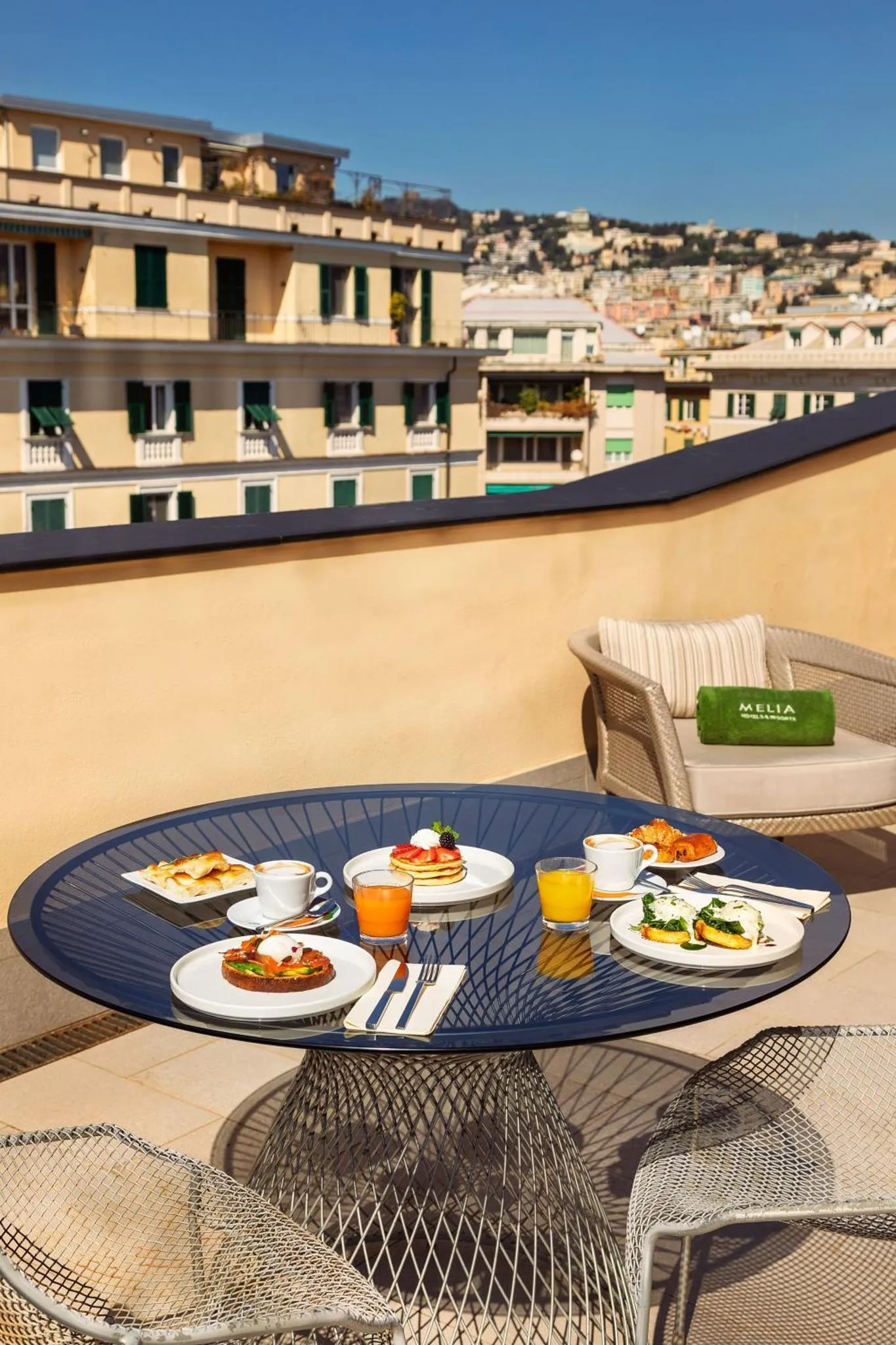 Une table ronde est dressée avec des plats et des boissons sur une terrasse ensoleillée.