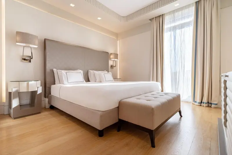 Une chambre lumineuse avec un grand lit et un banc au pied du lit.