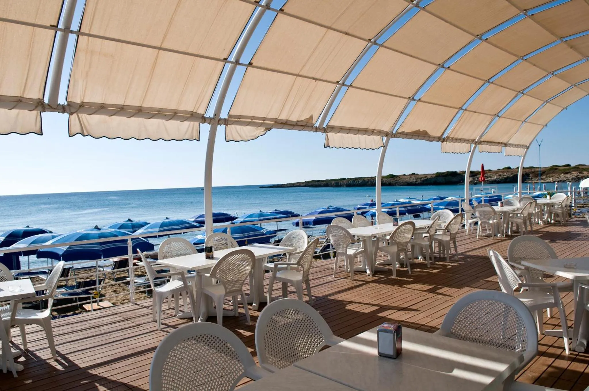 Terrasse ombragée avec tables et chaises donnant sur la mer.