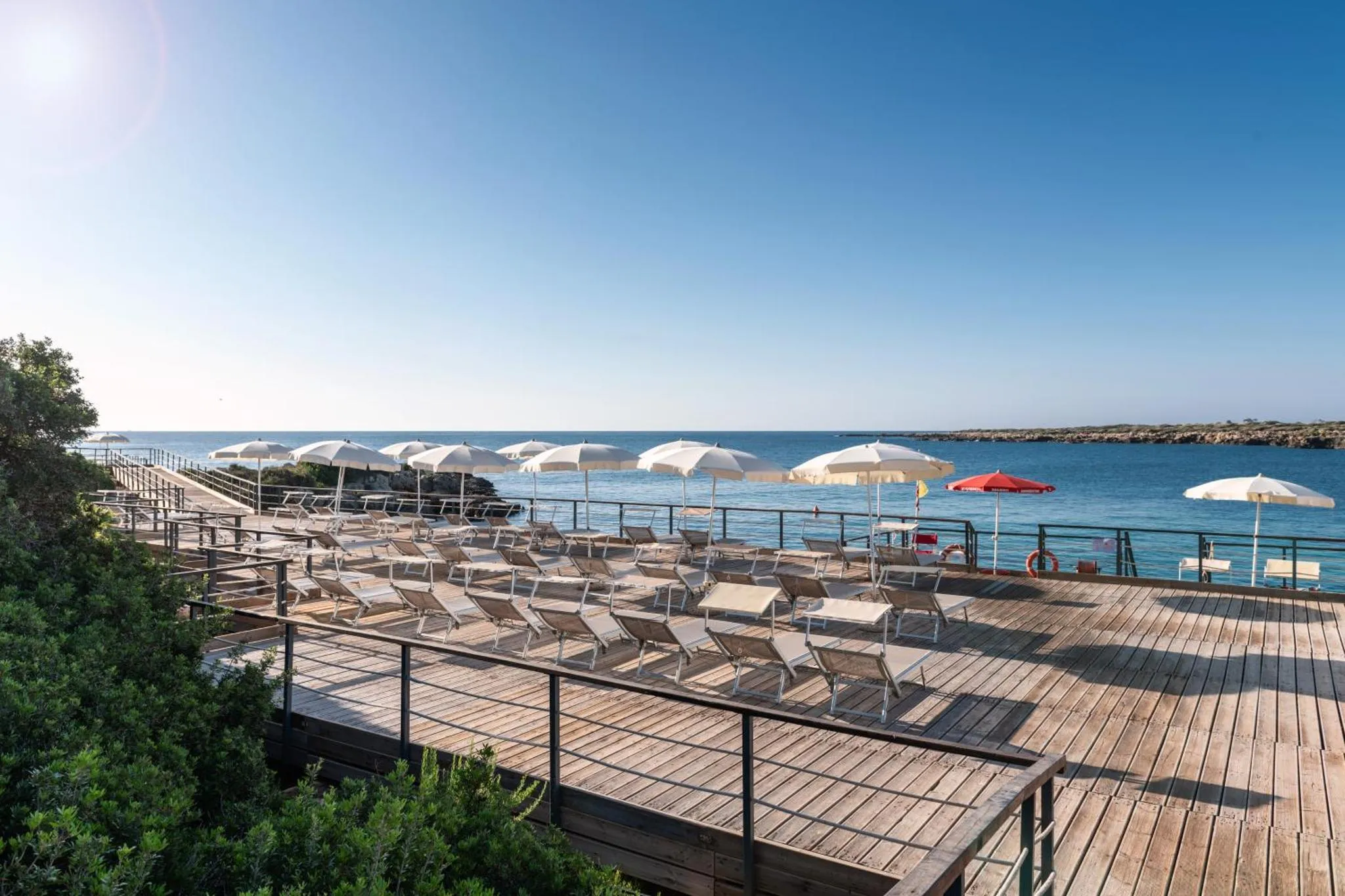Terrasse en bois avec transats blancs et parasols face à la mer.