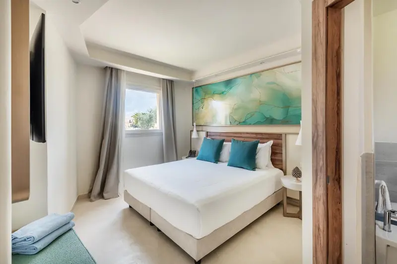 Une chambre lumineuse avec un grand lit et une décoration murale abstraite.