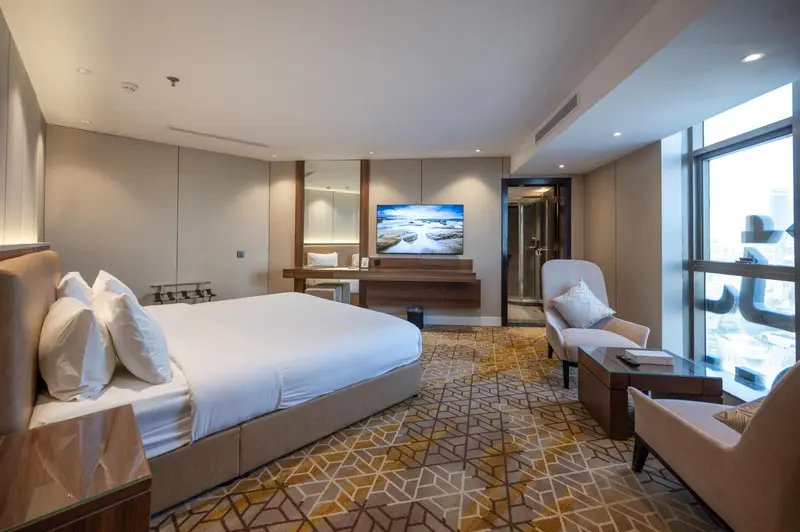 Chambre lumineuse avec un grand lit et un coin salon près d'une fenêtre.