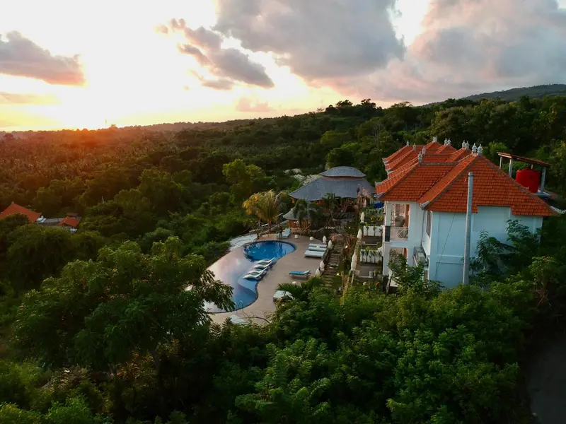 Vue aérienne d'un complexe hôtelier avec piscine et végétation luxuriante au coucher du soleil.