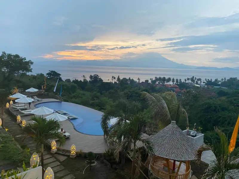 Vue panoramique sur une piscine et la mer au coucher du soleil.