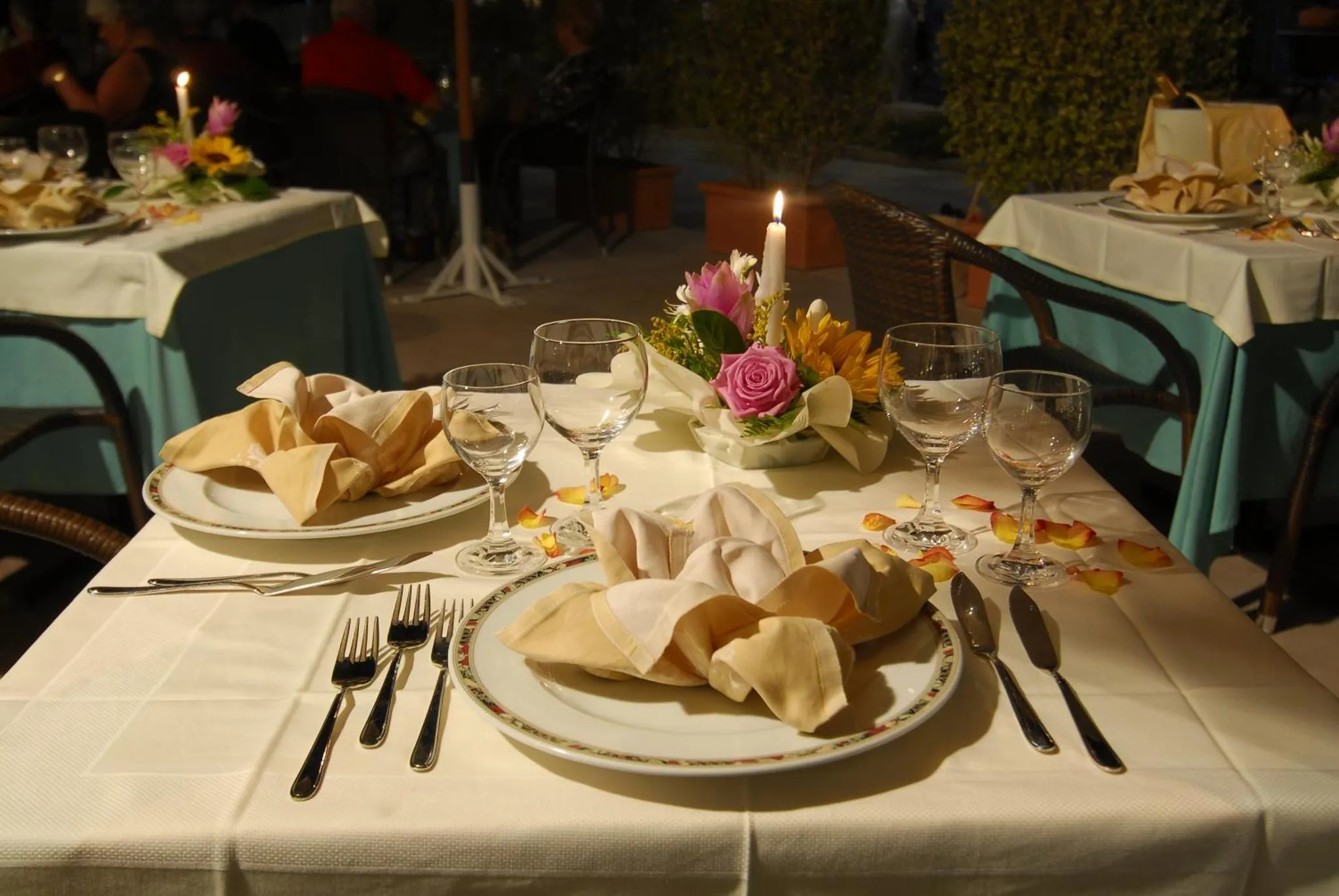 Une table dressée pour un repas en extérieur, décorée de fleurs et de bougies.