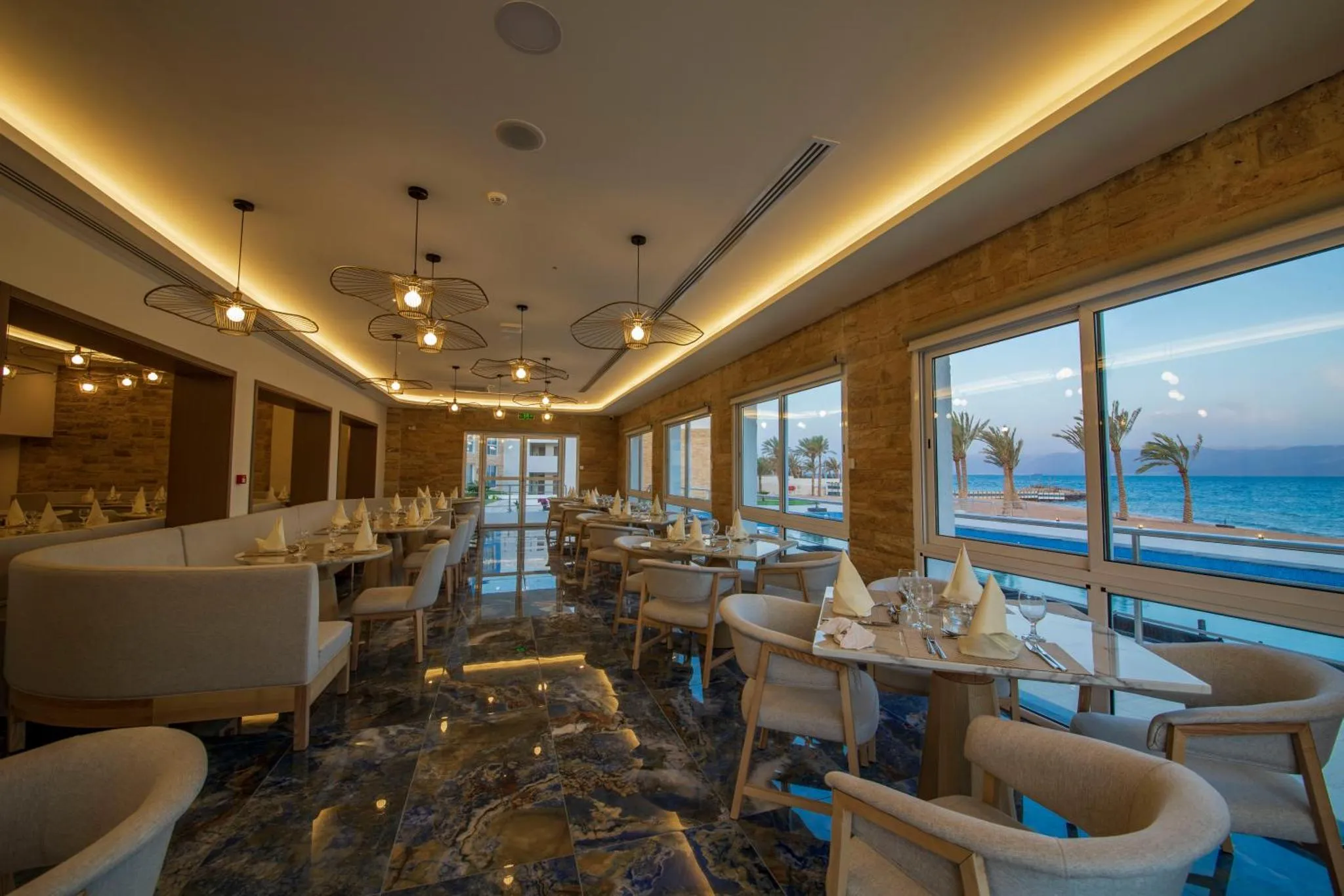 Une salle lumineuse avec des tables dressées face à une vue sur la mer.