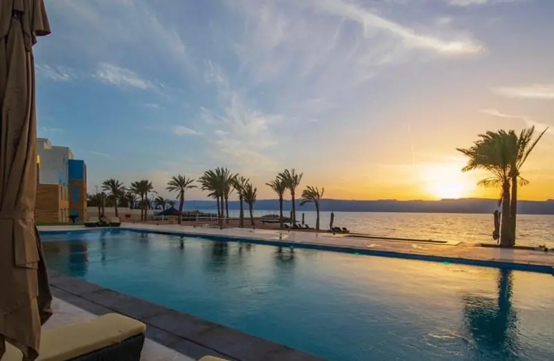 Une piscine turquoise reflète le ciel orangé au coucher du soleil.