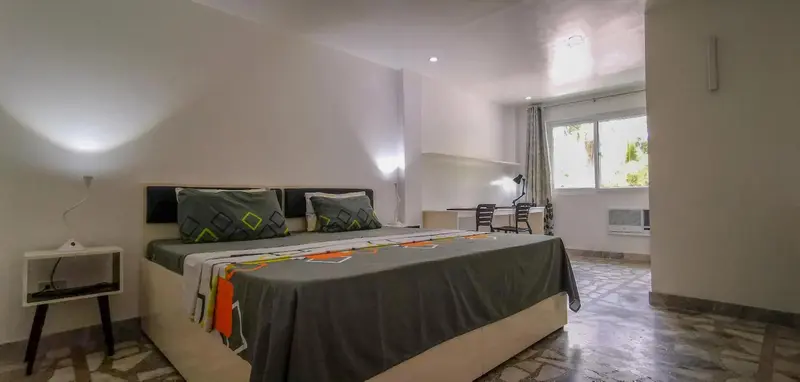 Une chambre lumineuse avec un grand lit et un bureau près d'une fenêtre.
