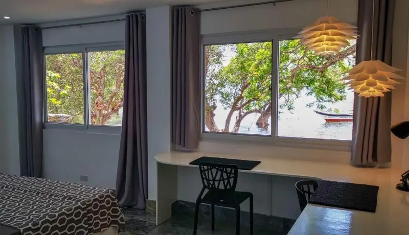 Une chambre lumineuse avec un bureau donnant sur la végétation et la mer.