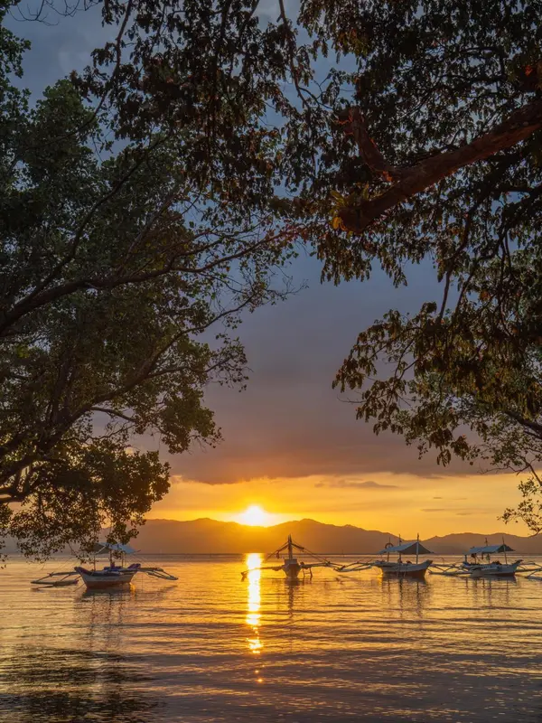 Le soleil se couche sur la mer, illuminant les bateaux à l'horizon.