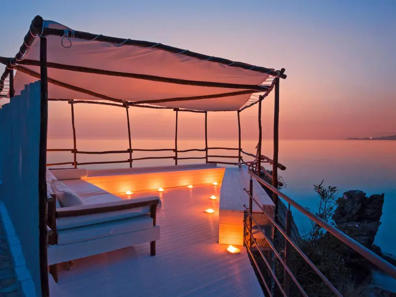 Terrasse lumineuse avec mobilier blanc surplombant la mer au coucher du soleil.