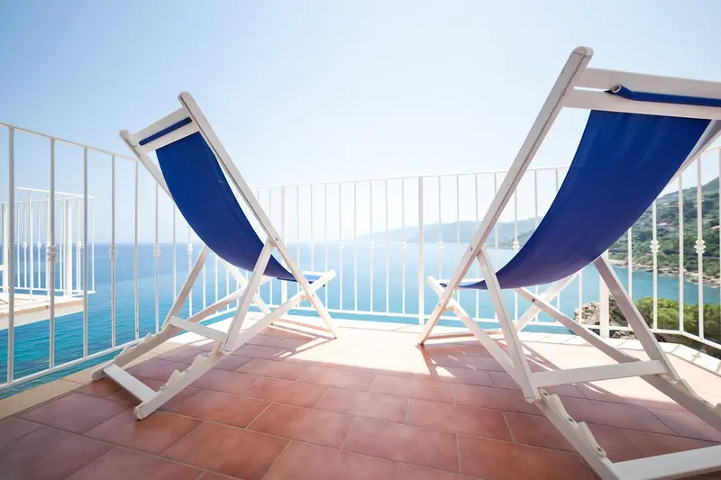 Deux chaises longues bleues sur une terrasse ensoleillée avec vue sur la mer.