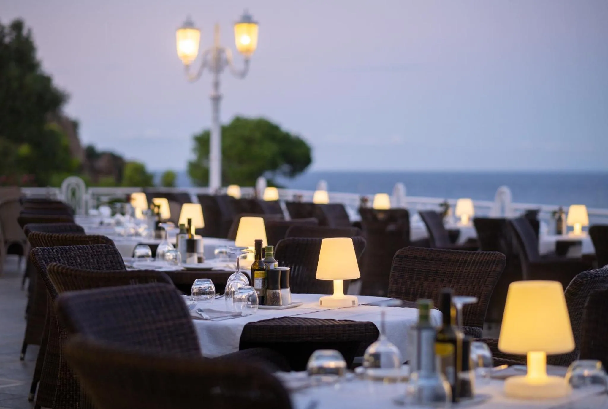 Tables dressées en terrasse avec vue sur la mer au crépuscule.