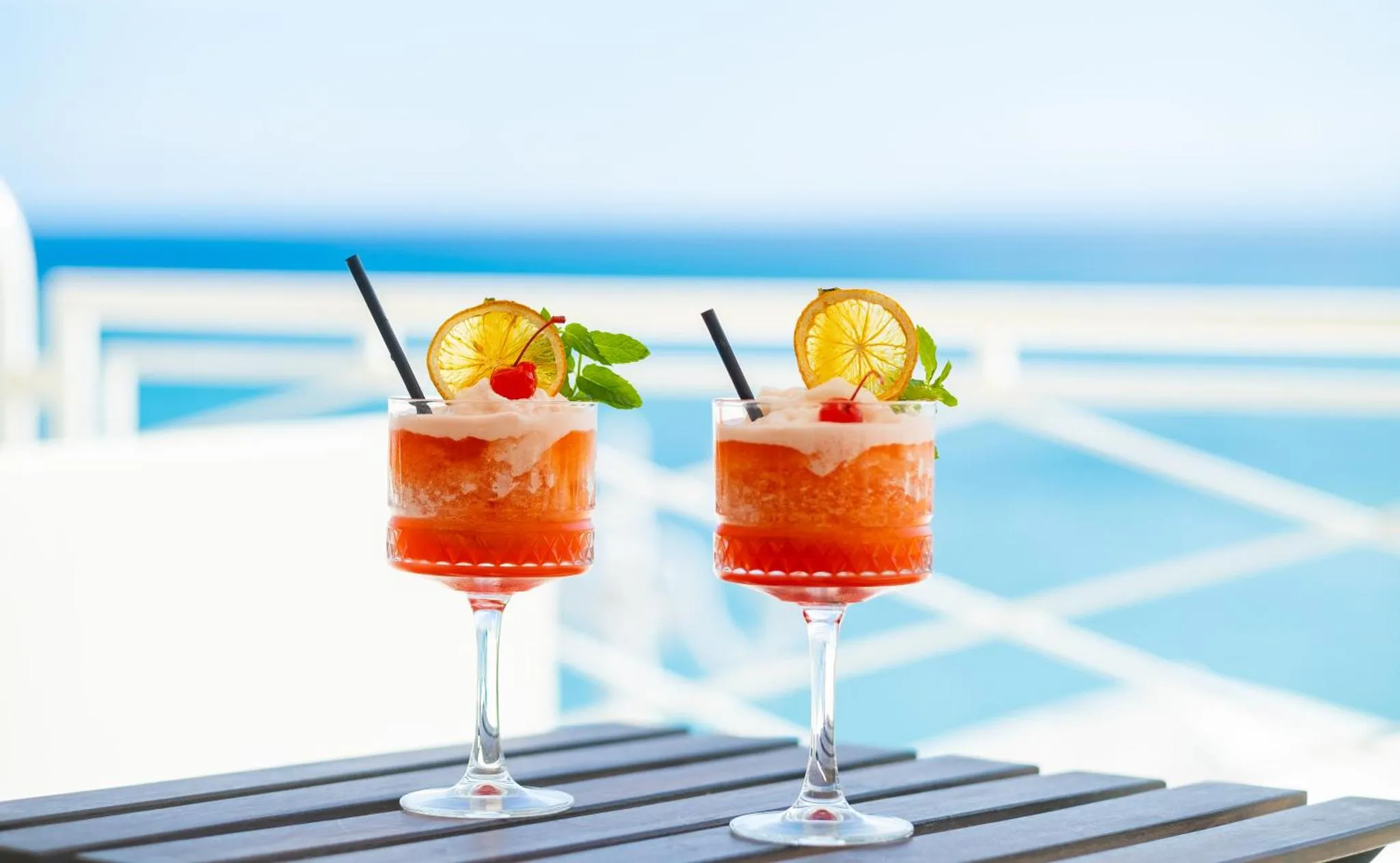 Deux cocktails colorés sont servis sur une table en bois face à la mer.