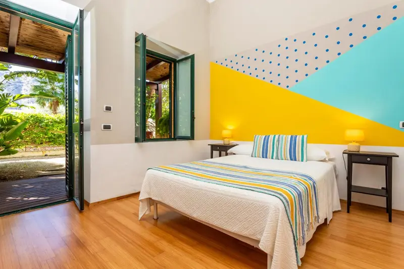 Chambre lumineuse avec un lit recouvert d'une courtepointe colorée et un accès à une terrasse.