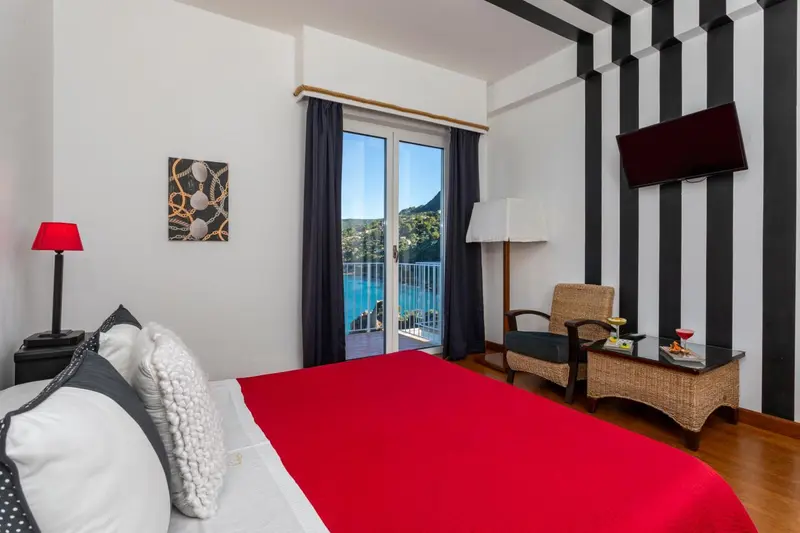 Une chambre lumineuse avec un lit rouge et un fauteuil en osier.
