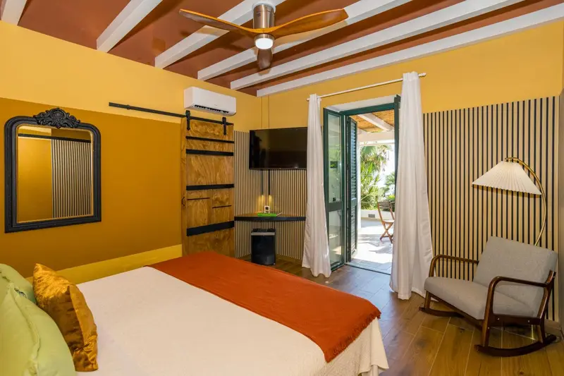 Une chambre lumineuse avec un lit recouvert d'une couverture orange et un fauteuil en bois.