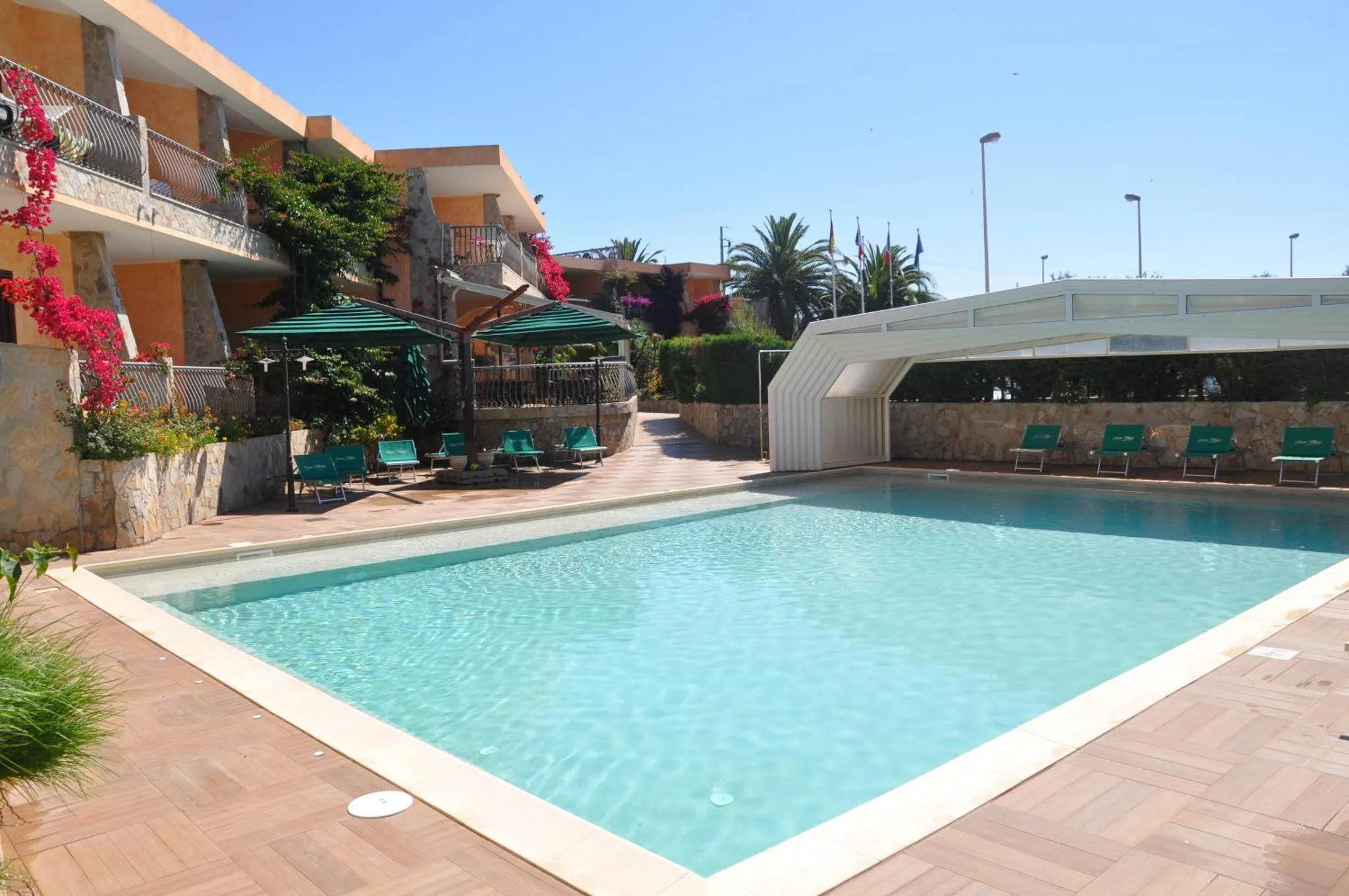 Une piscine rectangulaire turquoise entourée d'une terrasse carrelée et de transats verts.