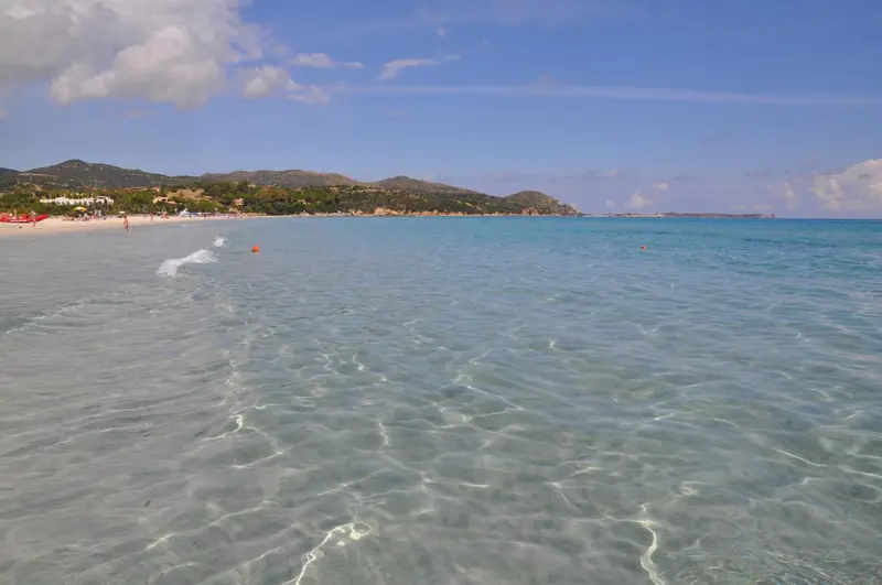 Vue d'une plage de sable blanc bordée d'une eau turquoise et de collines verdoyantes.
