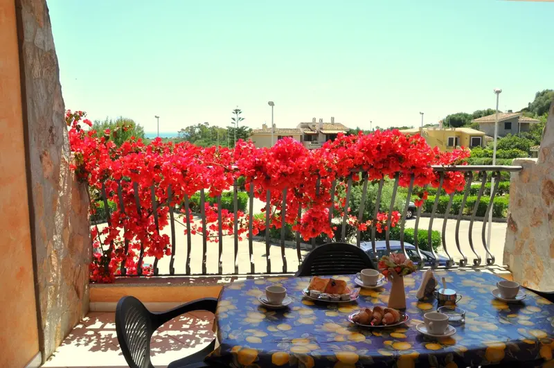 Une table avec un petit déjeuner est mise en scène sur une terrasse fleurie avec vue sur la mer.